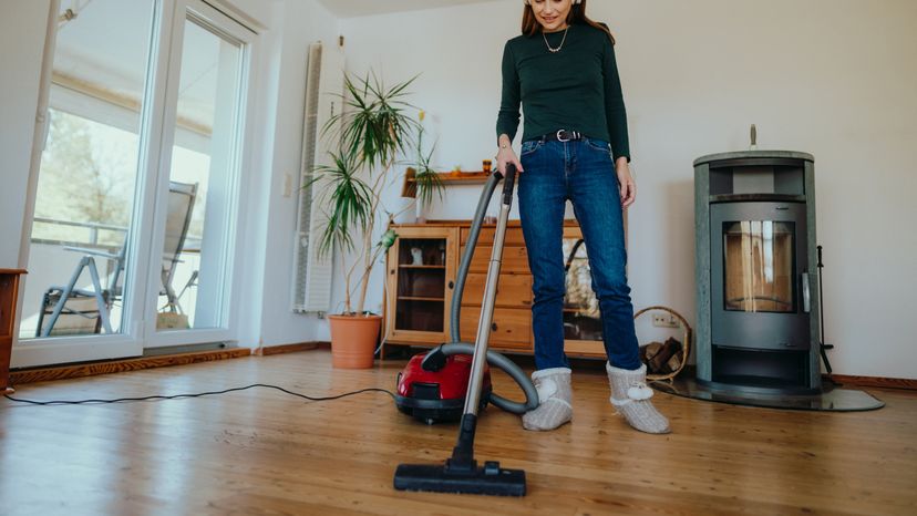 Young woman using wireless headphones to listen to a podcast while vacuuming and cleaning her home