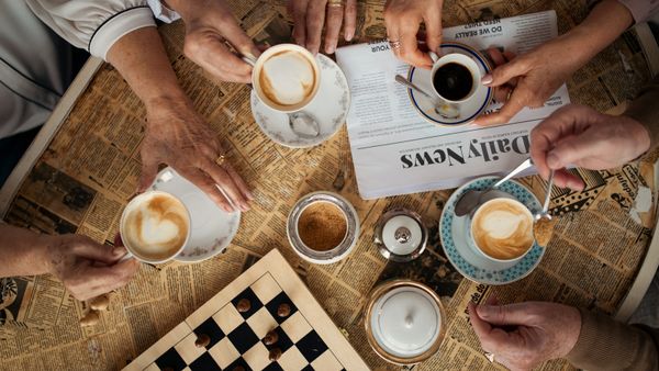 Top view of unrecognizable people sitting at table and having coffee together in café.