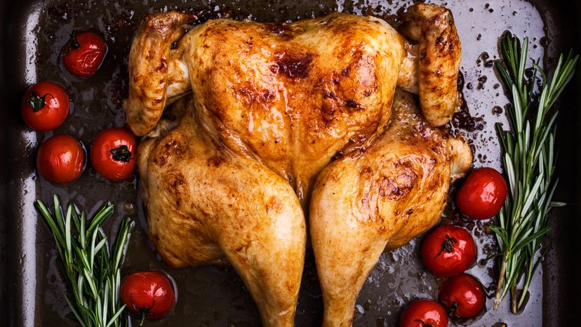 Butterflied roast chicken with  tomatoes and rosemary on baking sheet viewed from above