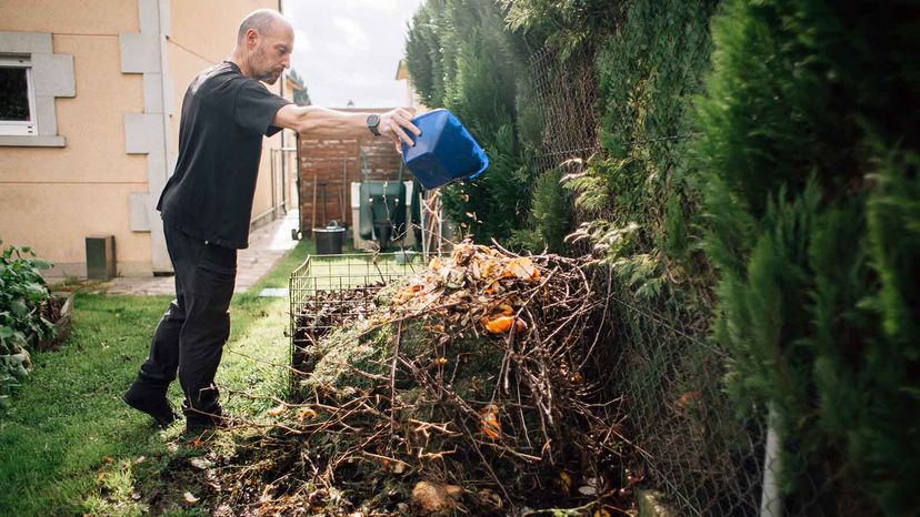 A man dumps a bowl of kitchen scraps in an outdoor compost pile.