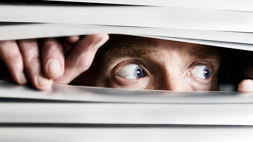 Terrified man looking out blinds