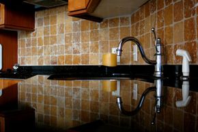 A shiny black kitchen countertop reflecting a silver faucet.
