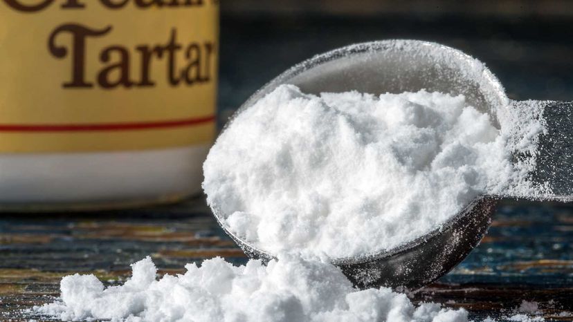 A measuring spoon full of cream of tartar powder, with the jar in the background.