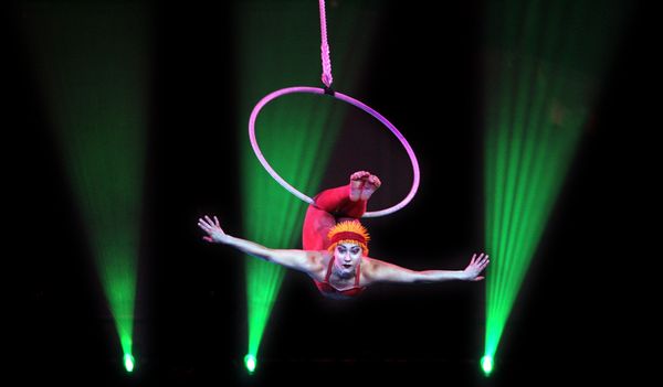 An aerialist swings on a hoop.