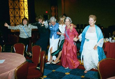 Women in dresses smiling on stage in performance space.