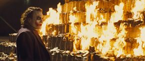 Heath Ledger as &quot;The Joker&quot; watches as piles of money burns.