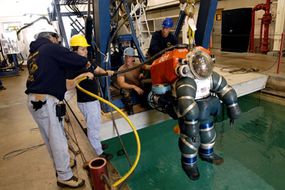 The Atmospheric Dive Suit (ADS) is lowered into the water for a dive.