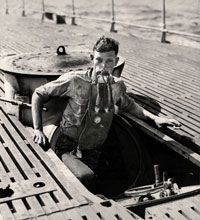 USS V-5 (SC 1) crewman A. L. Rosenkotter exits the submarine's escape hatch wearing the "Momsen Lung" emergency escape breathing device during sea trials.”border=