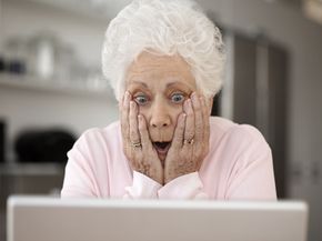 Senior woman looking at laptop with head in hands and open mouth 