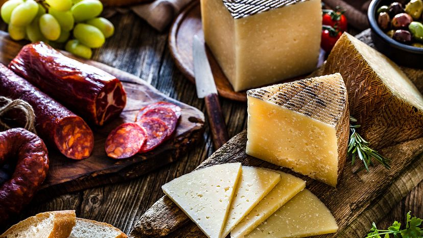 Manchego cheese pieces surrounded by Spanish chorizo, olives, bread slices and grapes. 