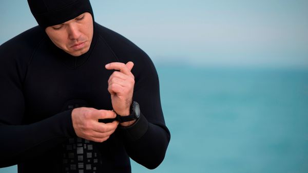 A diver in wetsuit putting a waterproof diver's watch