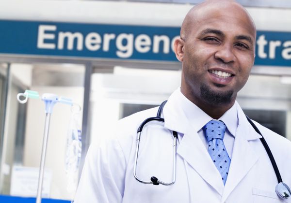 A doctor stands in front of a hospital exterior.