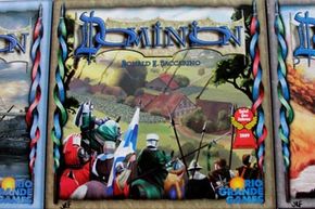 The front cover of the Dominion box, with artwork by Matthias Catrein. The game is flanked by expansions Seaside and Intrigue. We can't promise your friends will all love the game so much that you'll have to initial your copies like a summer camp towel. See more pictures of toys and games.