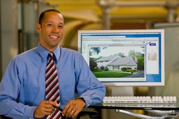 Man in front of computer screen showing picture of house