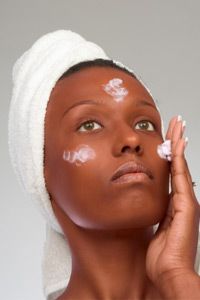 African-American girl applying facial skincare product (gray background)