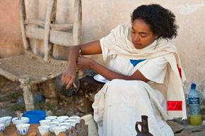 A woman in traditional Ethiopian dress pours coffee into small cups.