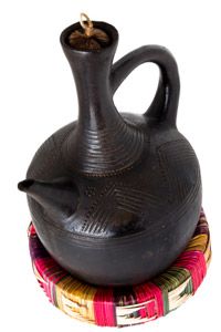 A long-necked clay coffee pot sitting on a colorful straw rest.