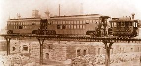 This circa 1877 view of a New York Elevated Railroad train is notable for the decorous steam dummy locomotive no. 18, Brooklyn, built by Brooks Works that year. These machines had centrally-located cylinders and a water tank atop the boiler.