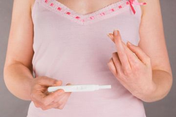 woman with pregnancy test crossing fingers