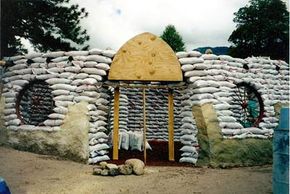 This earthbag home has a wooden door form and wagon wheel window forms.