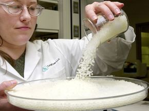 A quality assurance analyst pours pellets of corn plastic into a dish.