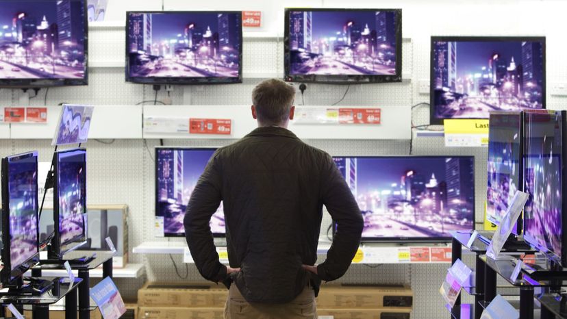 Man standing in front of ten modern televisions showing the same image.