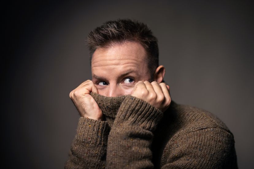 Close-up of a young man pulling a sweater over his face.