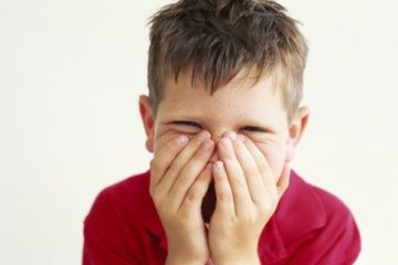 Boy (6-9) covering face with hands