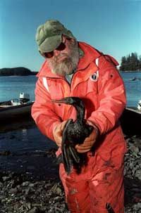 A fisherman carries a bird coated with oil that spilled from the Exxon Valdez tanker that ruptured off of the Alaskan coast.