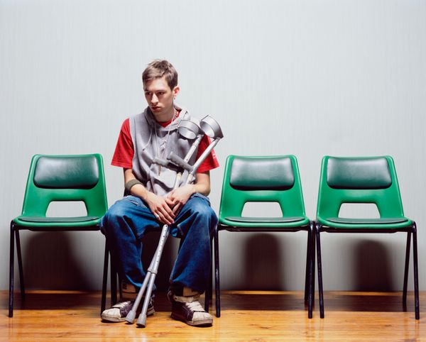 A man with crutches sits alone on chairs.