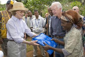 总统吉米·卡特（Jimmy Carter）和妻子罗莎琳（Rosalynn）在埃塞俄比亚西南部的偏远村庄阿菲塔（Afeta）逃出了防止疟疾的杀虫床网。“border=