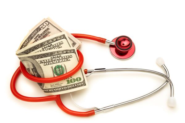A handful of $100 bills surrounded by a stethoscope.