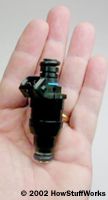A fuel injector in the palm of someone's hand.