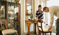 A man and a woman look at a vintage chair in an antique store.