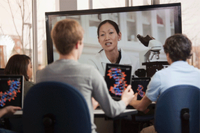 students with tablets watching female teacher on monitor