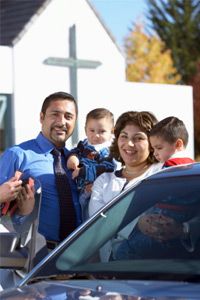 Mother, father and two sons (12 months-3) beside car outside church