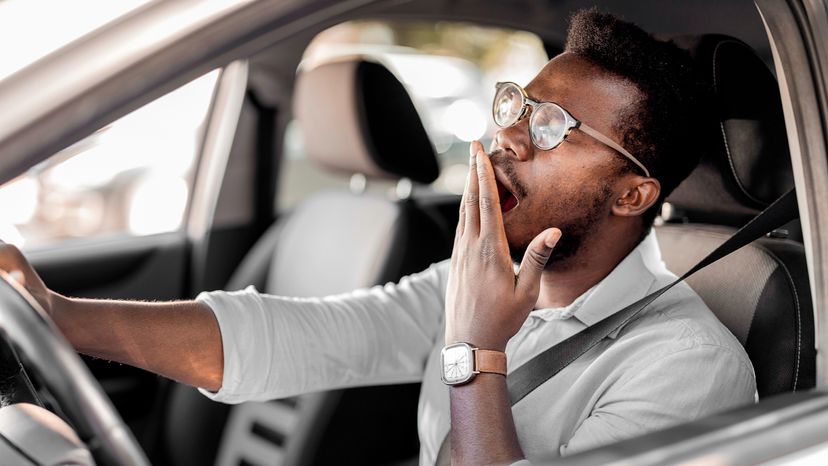 Sleepy fatigued yawning exhausted young man driving his car in traffic after a long hour drive. 