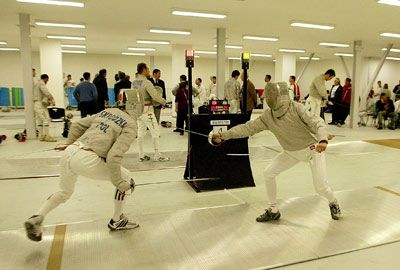 Fencers duel indoors with swords and masks.