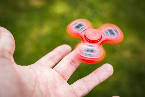 Close up of a bright red fidget spinner spinning on a man's index finger