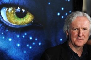 James Cameron poses in front of an "Avatar" poster. 