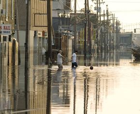 人们淹没了新奥尔良的道路行走在决堤的卡特里娜飓风风暴潮造成的。看到更多的风暴图片。”width=