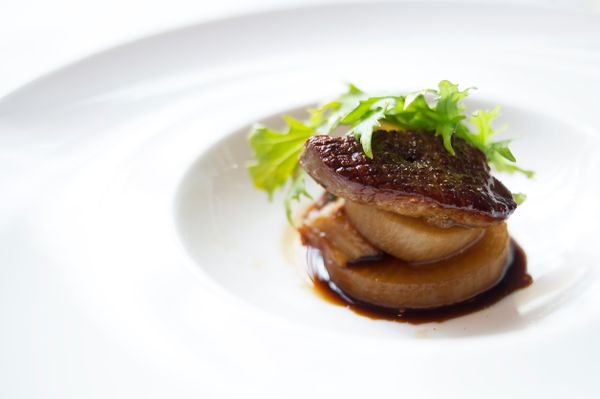 A caramelized slice of foie gras sits atop a piece of daikon radish in a pool of dark sauce.
