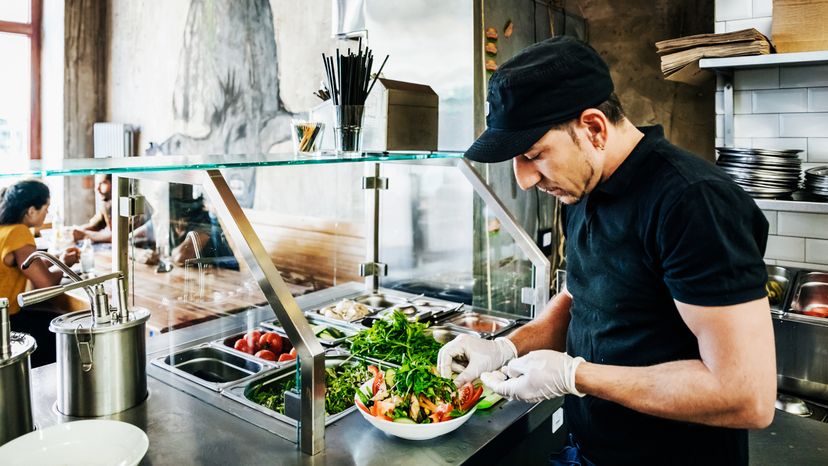 A chef preparing a salad dish for a customer in his trendy burger restaurant.