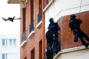 A French police intervention unit takes position outside a Paris apartment while a drone flies outside windows.