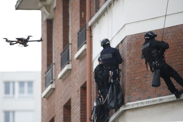 A drone hovers outside a high apartment window as police rappel from wires down the wall.