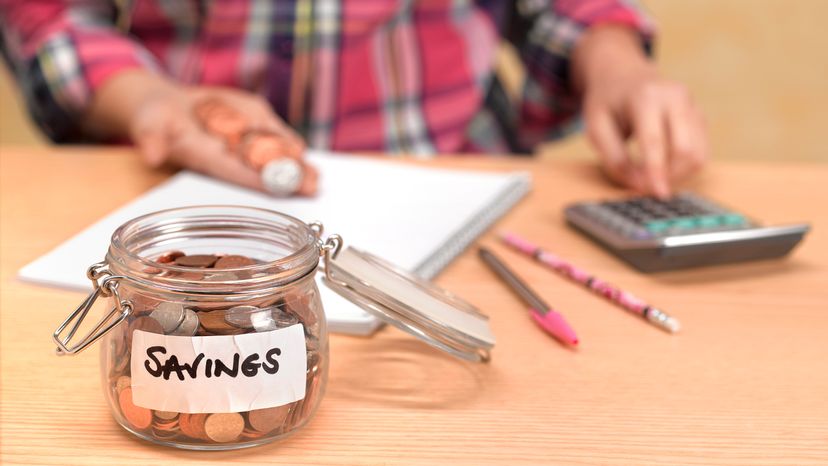Woman counting pennies with savings jar on table
