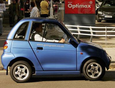 England's most popular electric car, the G-Wiz, drives past a petrol station in the background  in London.