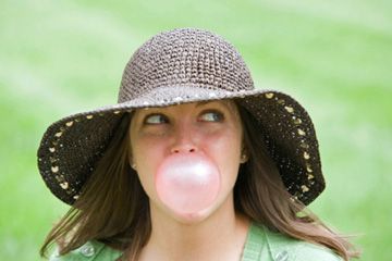 Blowing bubble in outdoor sun, adult alone.