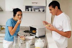 Two people in a kitchen enjoy a meal from a toaster oven.