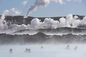 Visitors soothe themselves in a geothermal spa in Grindavik, Iceland while, in the distance, a power plant transforms the rising steam into electrical power.